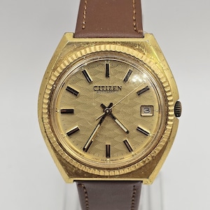 May include: Vintage Citizen Automatic watch with a gold-toned case and a brown leather strap. The watch face is gold with black markers and hands. The watch displays the date and the Citizen logo.