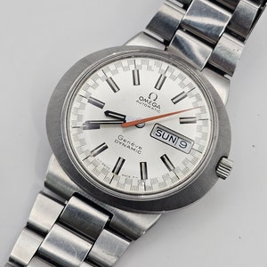 May include: A silver Omega Geneve Dynamic automatic wristwatch with a white face, black hour and minute hands, a red second hand, and a date window displaying "SUN 9".