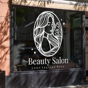 Puede incluir: Un escaparate muestra un logotipo ovalado blanco con el perfil de una mujer y detalles florales. Las palabras "Beauty Salon" y "your tagline here" están debajo. El exterior del edificio es de ladrillo.