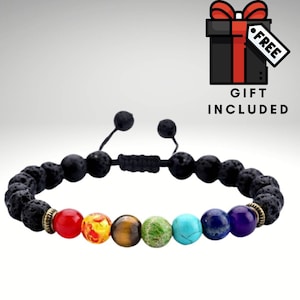 May include: A black lava stone bracelet with seven chakra beads. The beads are red, orange, yellow, green, blue, indigo, and violet. The bracelet has a black cord with a sliding knot for adjusting the size.  "Free Gift Included" is written on a red and black gift box.