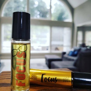 May include: Two amber glass roller bottles with black caps. The bottle on the left has a label with the word "FOCUS" in orange and a pair of eyeglasses. The bottle on the right has a gold label with the word "Focus" in black.