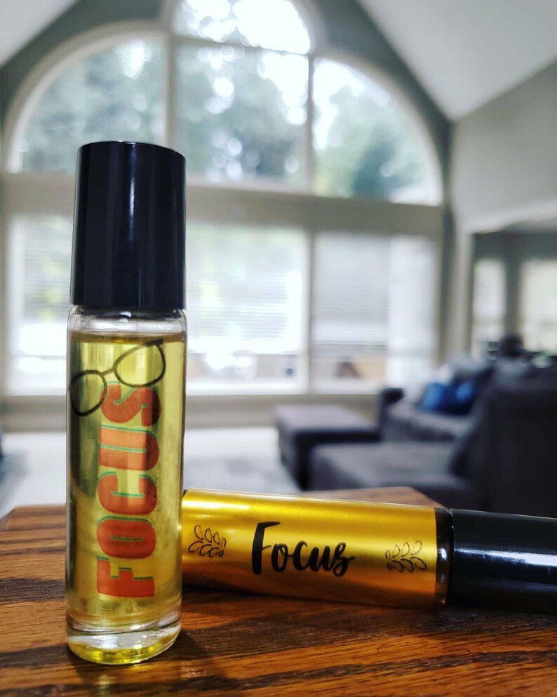 May include: Two amber glass roller bottles with black caps. The bottle on the left has a label with the word "FOCUS" in orange and a pair of eyeglasses. The bottle on the right has a gold label with the word "Focus" in black.