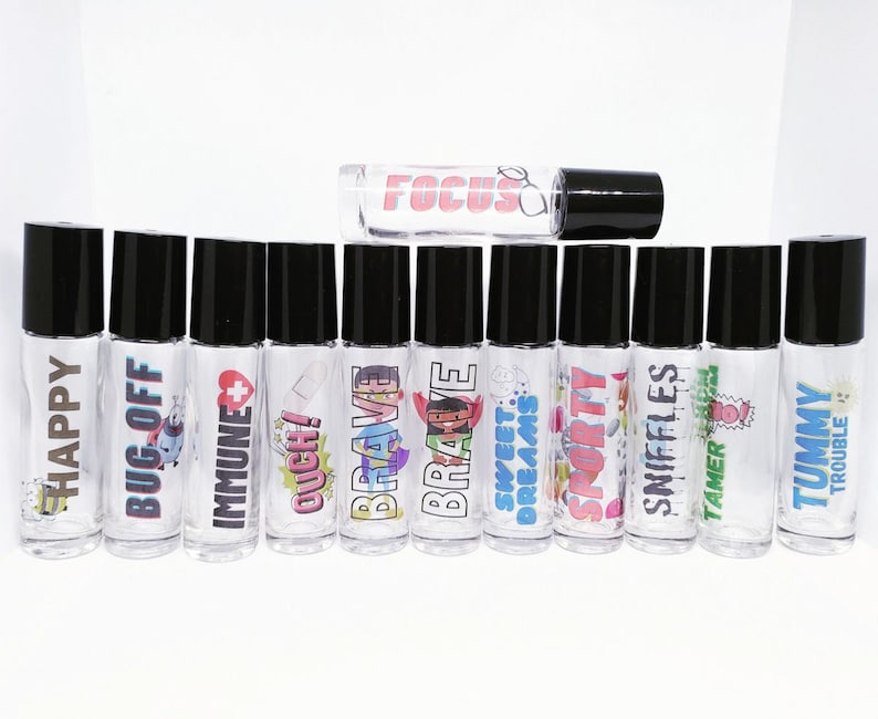 May include: A set of 12 clear glass roller bottles with black caps and colorful labels. The labels feature various phrases and images, including "Happy", "Bug Off", "Immune", "Ouch!", "Brave", "Sweet Dreams", "Sporty", "Sniffles", "Tamer", "Tummy", and "Trouble".