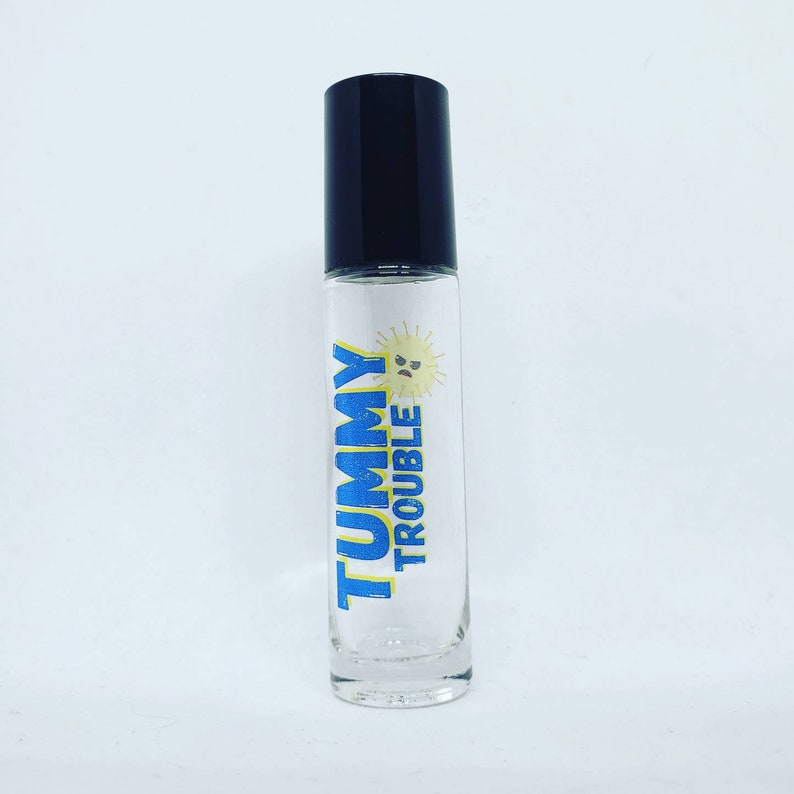 May include: A clear glass roller bottle with a black cap. The bottle has a yellow sun with a frowning face and the text "TUMMY TROUBLE" in blue.