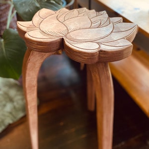 K&ouml;nnte beinhalten: Ein Holzhocker mit einem in die Oberseite geschnitzten Lotusblumenmuster. Der Hocker hat zwei Beine, die sich nach au&szlig;en und dann wieder nach innen biegen.