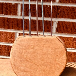 May include: A wooden stand with six metal crochet hooks. The stand is brown and has a rounded shape. The hooks are silver and have different sizes.