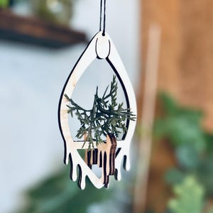 May include: A wooden hanging planter with a drip design, featuring a small green plant inside. The planter is made of light wood and has a simple, modern design.