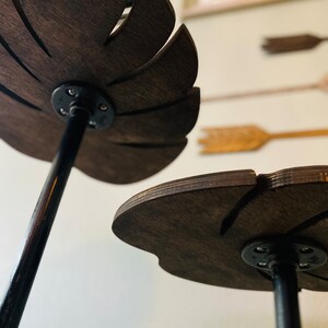 May include: Two wooden leaf-shaped shelves with black metal stands. The shelves are dark brown and have a natural wood grain. The stands are simple and sturdy.
