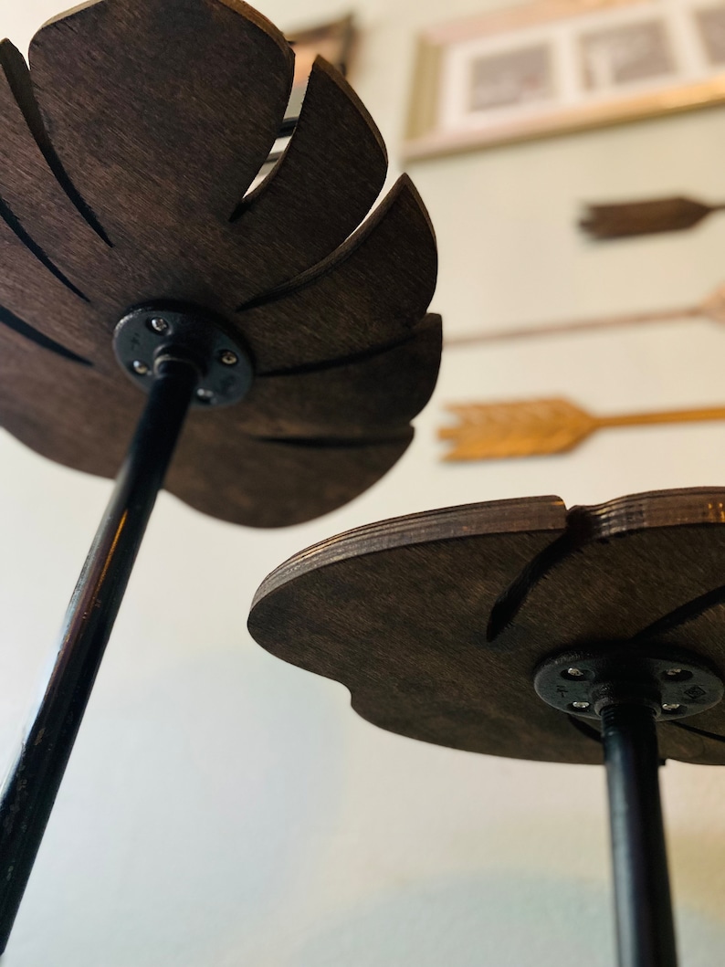 May include: Two wooden leaf-shaped shelves with black metal stands. The shelves are dark brown and have a natural wood grain. The stands are simple and sturdy.