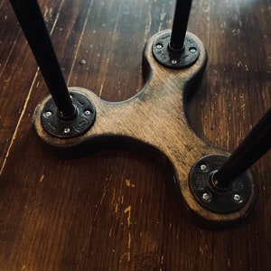May include: A wooden table base with three black metal legs. The legs are attached to the base with round metal plates and screws.