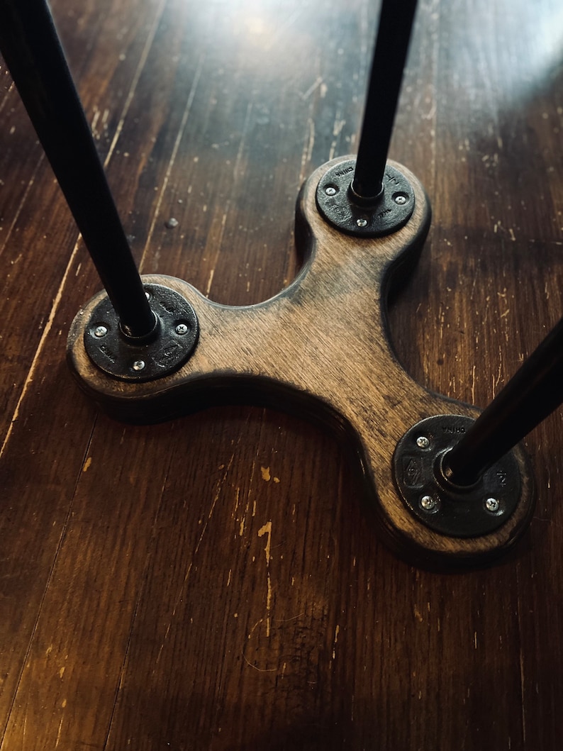May include: A wooden table base with three black metal legs. The legs are attached to the base with round metal plates and screws.