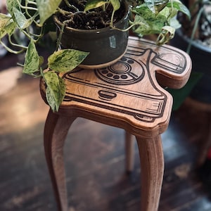 May include: A wooden stool with a vintage rotary phone design. The stool has three legs and is topped with a potted plant.