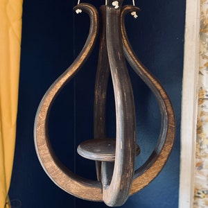 May include: A dark brown wooden hanging planter with a circular design and a small platform in the center. The planter is suspended by three white cords.