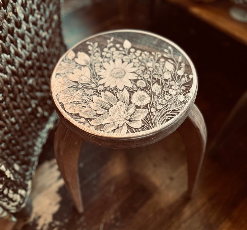 May include: A wooden stool with a carved floral design. The design features white flowers and leaves on a brown background.