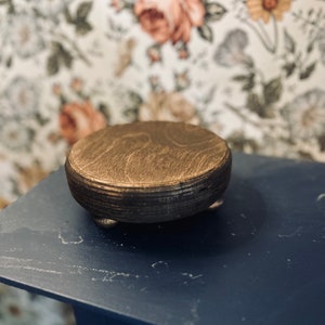 May include: A round wooden pedestal with a gold finish and three legs. The pedestal is sitting on a blue surface.
