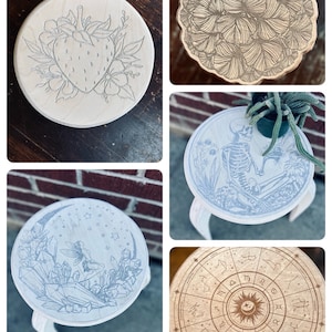 May include: Four different wooden stools with various designs. The first stool has a strawberry and flowers design. The second stool has a floral design. The third stool has a skeleton and flowers design. The fourth stool has a zodiac wheel design.