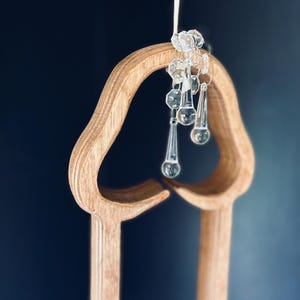 May include: A wooden cutout of a heart shape with a string of crystal beads hanging from the top. The beads are clear and have a teardrop shape.