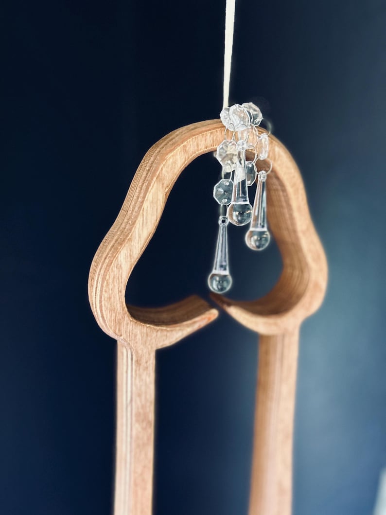 May include: A wooden cutout of a heart shape with a string of crystal beads hanging from the top. The beads are clear and have a teardrop shape.
