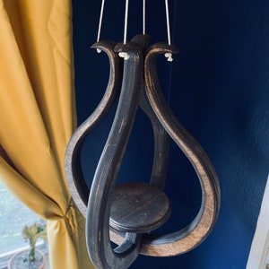 May include: A dark brown wooden hanging planter with a circular base and a unique, intertwined design. The planter is suspended by three white cords.