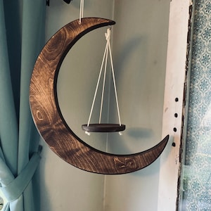 May include: A wooden crescent moon wall hanging with a small circular wooden shelf suspended from it by white cords.