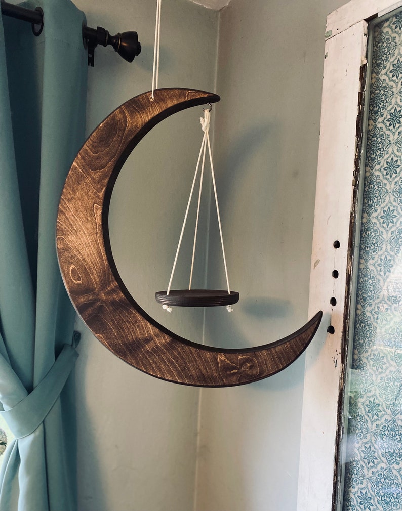 May include: A wooden crescent moon wall hanging with a small circular wooden shelf suspended from it by white cords.