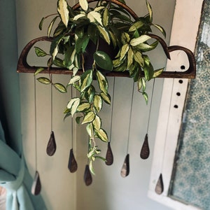 Może przedstawiać: Drewniany, chmurowy kwietnik z wiszącą rośliną. Kwietnik jest ciemnobrązowy i zawieszony na suficie. Roślina ma zielono-białe, pstre liście i opada w dół kaskadą. Kwietnik ma małe, drewniane ozdoby w kształcie łez, które wiszą.