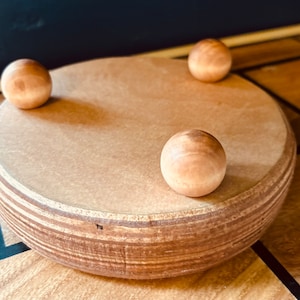 May include: A wooden spinning top with three wooden balls on the bottom. The top is made of light brown wood and has a natural finish.
