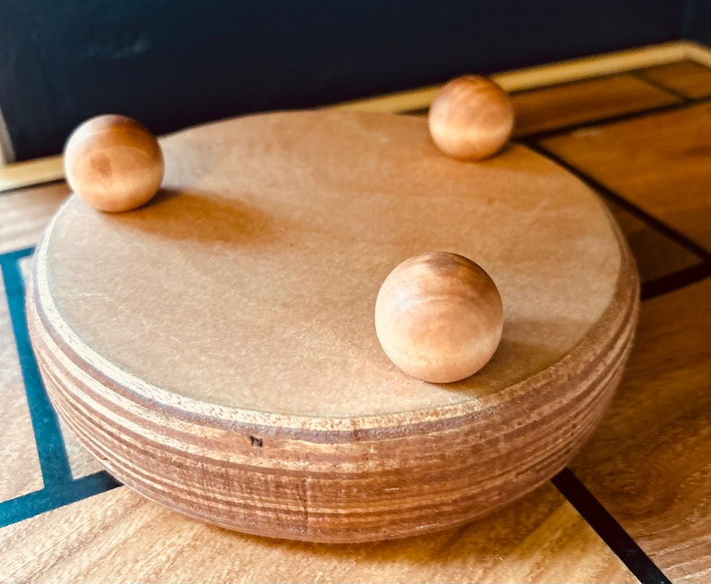 May include: A wooden spinning top with three wooden balls on the bottom. The top is made of light brown wood and has a natural finish.