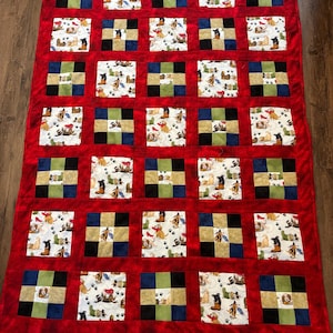 May include: A handmade quilt with a red border and a patchwork design. The quilt features squares with dog-themed fabric and alternating squares of solid colors, including black, blue, and green. The dog fabric has various dog breeds.