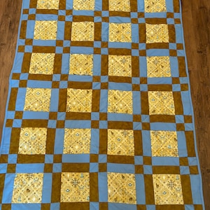May include: A blue and brown patchwork quilt with a repeating pattern of small squares. The quilt is made of different fabrics and has a rustic, vintage look.