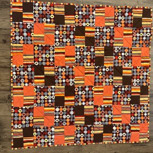 Könnte beinhalten: Eine Patchwork-Decke mit verschiedenen braunen, orangen und weißen Stoffen. Die Decke besteht aus Quadraten und Rechtecken, wobei jedes Stück ein anderes Muster hat. Die Decke ist perfekt, um jedem Raum einen Hauch von Wärme und Farbe zu verleihen.