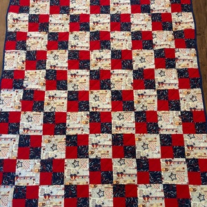 Op de afbeelding: Een rood, wit en blauw patchwork-deken met een geruit patroon. Het deken is gemaakt van verschillende stoffen met sterren, harten en andere patriottische ontwerpen.