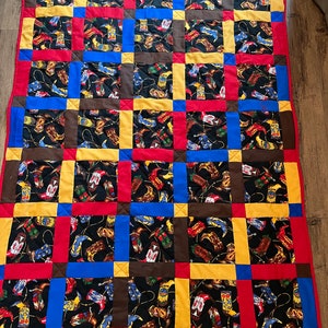 以下が含まれることがあります： カウボーイブーツの繰り返しパターンが描かれた黒い背景のキルト。キルトは赤、黄、青、茶色の正方形で構成されています。