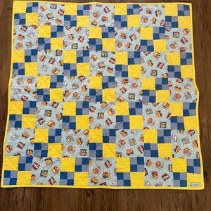 Door de lucht, over land of over zee is het thema voor deze schattige quilt. Auto's, boten, vliegtuigen, treinen en zelfs heteluchtballonnen staan op vintage postzegels.
