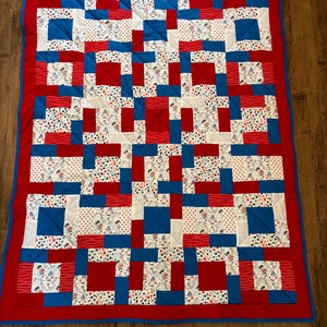 May include: A red, white, and blue patchwork quilt with a variety of patterns. The quilt is made up of squares and rectangles, and the colors are arranged in a random pattern. The quilt is edged in a blue and red trim.