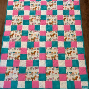Patchwork quilt met boerderijdieren, paarden, koeien, varkens, kippen, roze en turquoise blokken.