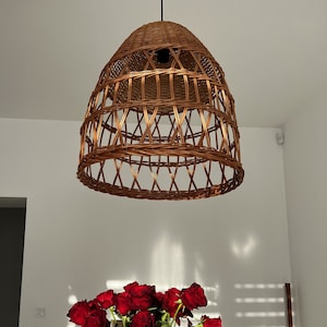 May include: A wicker pendant light hangs from the ceiling above a bouquet of red roses in a glass vase on a white table.