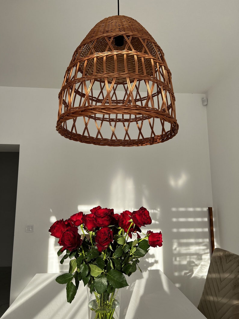 May include: A wicker pendant light hangs from the ceiling above a bouquet of red roses in a glass vase on a white table.