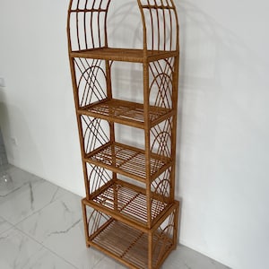 May include: A tall, arched, woven wicker shelf unit with four shelves. The shelf unit is made of natural brown wicker and has a rustic, bohemian style.