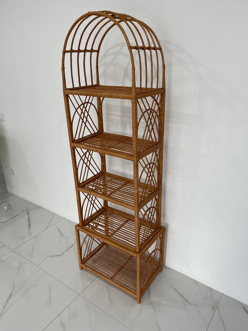 May include: A tall, arched, woven wicker shelf unit with four shelves. The shelf unit is made of natural brown wicker and has a rustic, bohemian style.