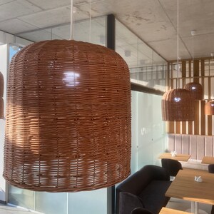 Puede incluir: Un interior de restaurante moderno con una l&aacute;mpara colgante de mimbre tejido colgando del techo. La luz es marr&oacute;n y tiene una forma redonda. Hay varias mesas y sillas en el fondo.