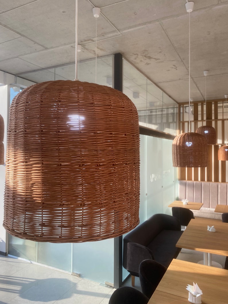 Puede incluir: Un interior de restaurante moderno con una l&aacute;mpara colgante de mimbre tejido colgando del techo. La luz es marr&oacute;n y tiene una forma redonda. Hay varias mesas y sillas en el fondo.