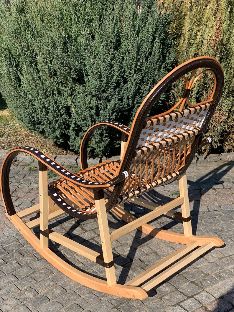 May include: A wooden rocking chair with a woven seat and back. The chair is brown and white with black accents. The chair is on a brick patio.