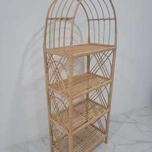 May include: A natural woven rattan shelf unit with an arched top and four shelves. The shelf unit is made of light brown rattan and has a natural finish.