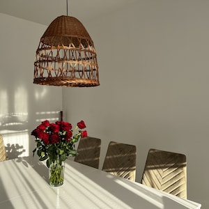May include: A white dining table with a wicker pendant light hanging above it.  There are four chairs around the table, and a vase of red roses in the center.