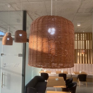 Puede incluir: Un comedor moderno con una mesa y sillas de madera clara. Tres l&aacute;mparas colgantes de mimbre cuelgan del techo. Las paredes son de color beige claro y hay una gran ventana en el fondo.