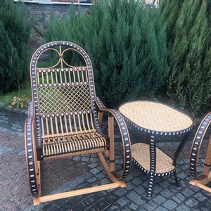May include: A set of two wicker rocking chairs with black and white trim and a matching wicker table with a black and white trim. The chairs and table are on a stone patio.
