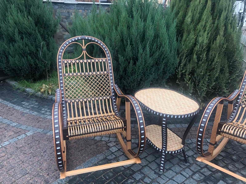 May include: A set of two wicker rocking chairs with black and white trim and a matching wicker table with a black and white trim. The chairs and table are on a stone patio.