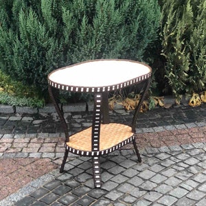 May include: A brown wicker side table with a white oval top and a lower shelf. The table has a unique design with black and white stripes around the edges.