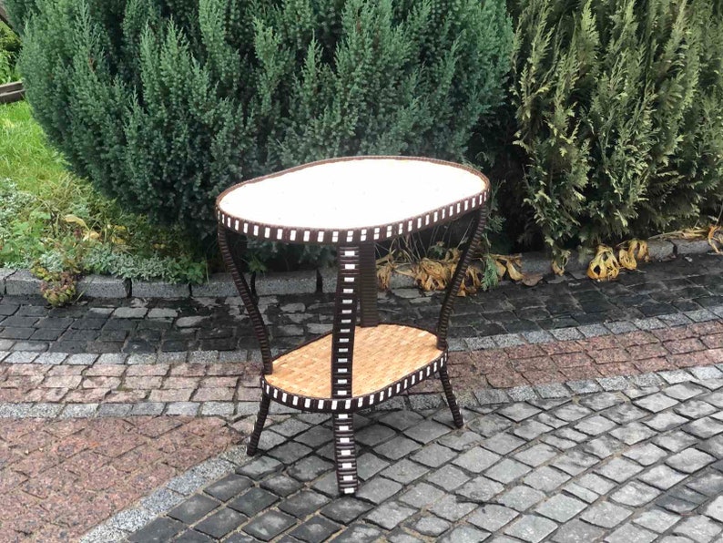 May include: A brown wicker side table with a white oval top and a lower shelf. The table has a unique design with black and white stripes around the edges.